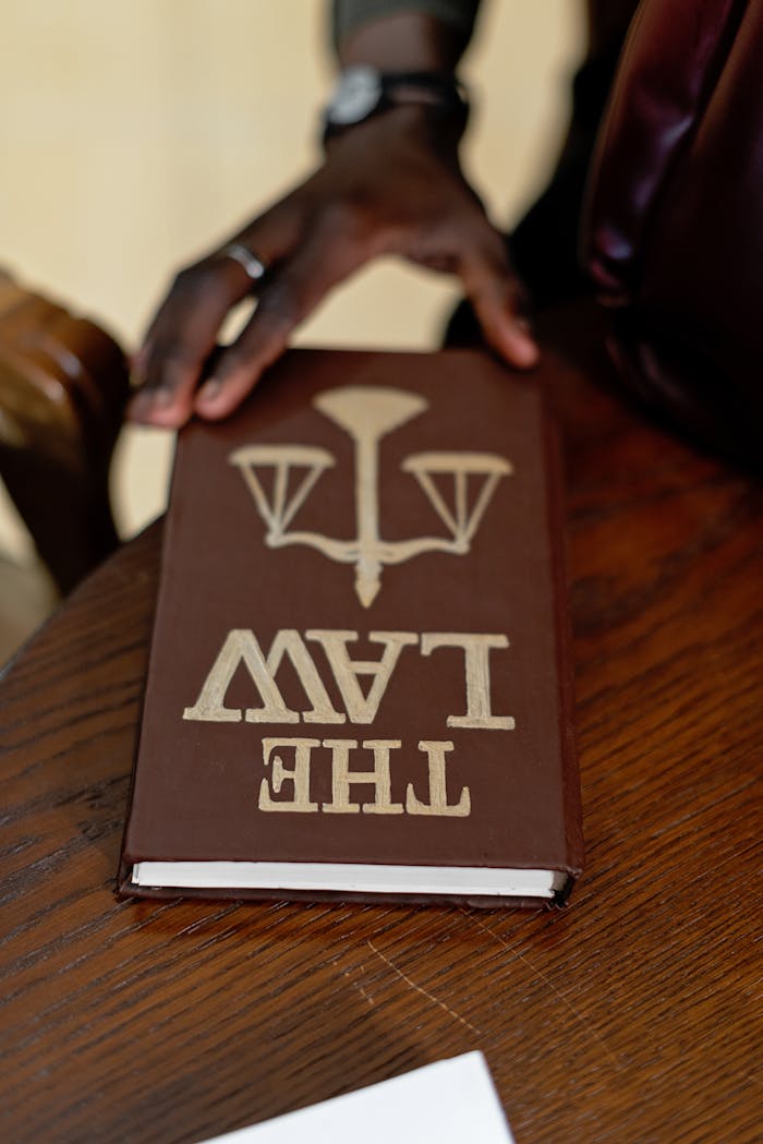 A close-up of a hand holding a law book on a wooden table, emphasizing legal studies.